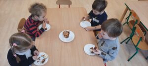Czworo dzieci siedzi przy stoliku. Jedzą wspólnie babeczki.