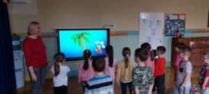 zdjęcie przedstawia grupę dzieci oglądającą prezentację multimedialną i wykonującą ćwiczenia logopedyczne.