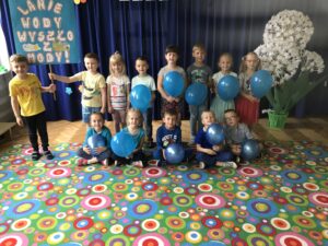 Na zdjęciu widać grupę przedszkolaków, trzymających niebieskie balony i transparent o wodzie.