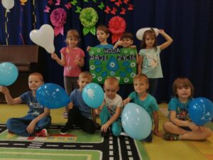 Na zdjęciu widać grupę przedszkolaków, trzymających niebieskie balony i transparent o wodzie.