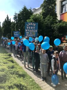 Na zdjęciu widać maszerujących przedszkolaków, trzymających niebieskie balony i transparenty o wodzie.