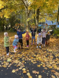 Dzieci bawią się jesiennymi liśćmi w czasie spaceru.