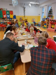 Przedszkolaki wraz z rodzicami siedzą przy stole i dekorują pierniczki
