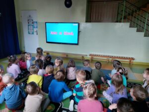 Przedszkolaki siedzą na dywanie I ogladaja prezentacje multimedialna 