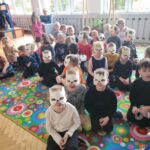 Dzieci przebrane w maski i stroje kota siedzą na dywanie.