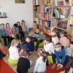 Dzieci zwiedzają bibliotekę. W tle widoczne regały z książkami.