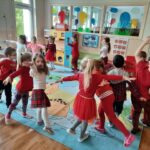 Dzieci stoją na dywanie, wykonują ruchy do tańca.