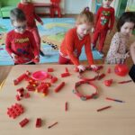 Dzieci segregują przy stoliku przedmioty w kolorze czerwonym.