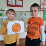 dzieci w pomarańczowych strojach prezentują wykonaną pracę