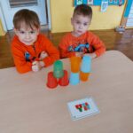 Dwóch chłopców siedzi przy stoliku. Bawią się w kodowanie przy wykorzystaniu kolorowych kubków.