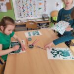 Grupa dzieci przy stoliku wykonuje zielone obrazki