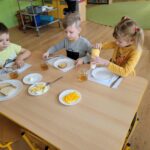 Troje dzieci siedzi przy stoliku i jedzą śniadanie