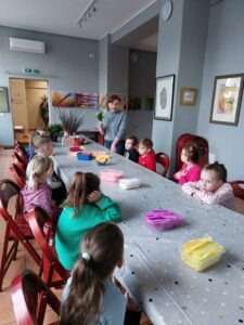 Dzieci siedzą przy stole i słuchają pracownika Muzeum na temat świąt Wielkanocnych 