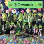 Grupa dzieci ubranych w zielone ubrania stoją na tle wystawy wiosennej