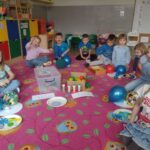 Dzieci siedzą na dywanie. Bawią się niebieskimi balonami.