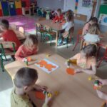 Dzieci wykonują przy stolikach prace plastyczne z pomarańczowych kół.