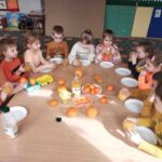 Grupa dzieci siedzi wokół stolika, na którym są pomarańcze