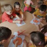 Dzieci wykonują w parach prace plastyczne w kolorze pomarańczowym.