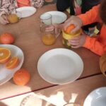 Dzieci zgromadzone wokół stoliczka wyciskają sok z pomarańczy