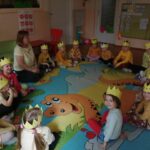 Dzieci siedzą w kręgu na dywanie w żółtych koronach na głowie