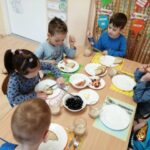 Dzieci siedzą przy stoliku. Spożywają posiłek w kolorze niebieskim
