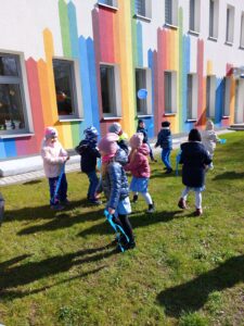 Przedszkolaki biegają z niebieskimi wstążkami po placu przedszkolnym