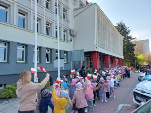 Przedszkolaki stoją pod Urzędem miasta w Radomsku i machają flagą Polski 