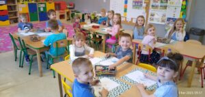 Przedszkolaki siedzą przy stolikach i kolorują obrazek na znak autyzmu 