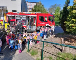 Dzieci stroją na placu przedszkolnym przed wozem strażackim 