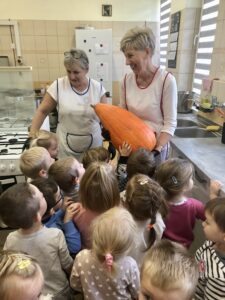 Dzieci i panie kucharki trzymające dużą dynie na zupę